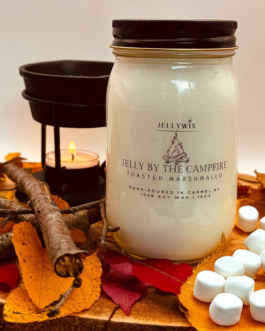 Jellywix candle labeled 'By the Campfire' with marshmallows and autumn leaves on a wooden surface.
